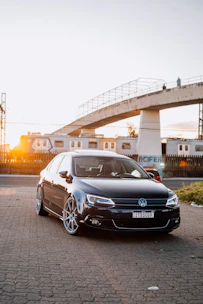 A sleek black car waiting outside a modern train station at dusk.