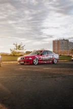 An outdoor shot of a customized old car with matte paint and rugged tires parked on a gravel road at sunset.