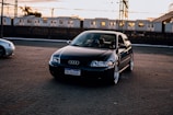 a black car parked in a parking lot next to a train