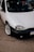 A close-up view of a parked white car with a clean and shiny exterior. The focus is on the front section of the car, showcasing its headlight, grille, and polished alloy wheel. The car is parked on an asphalt surface, with part of its registration plate visible.
