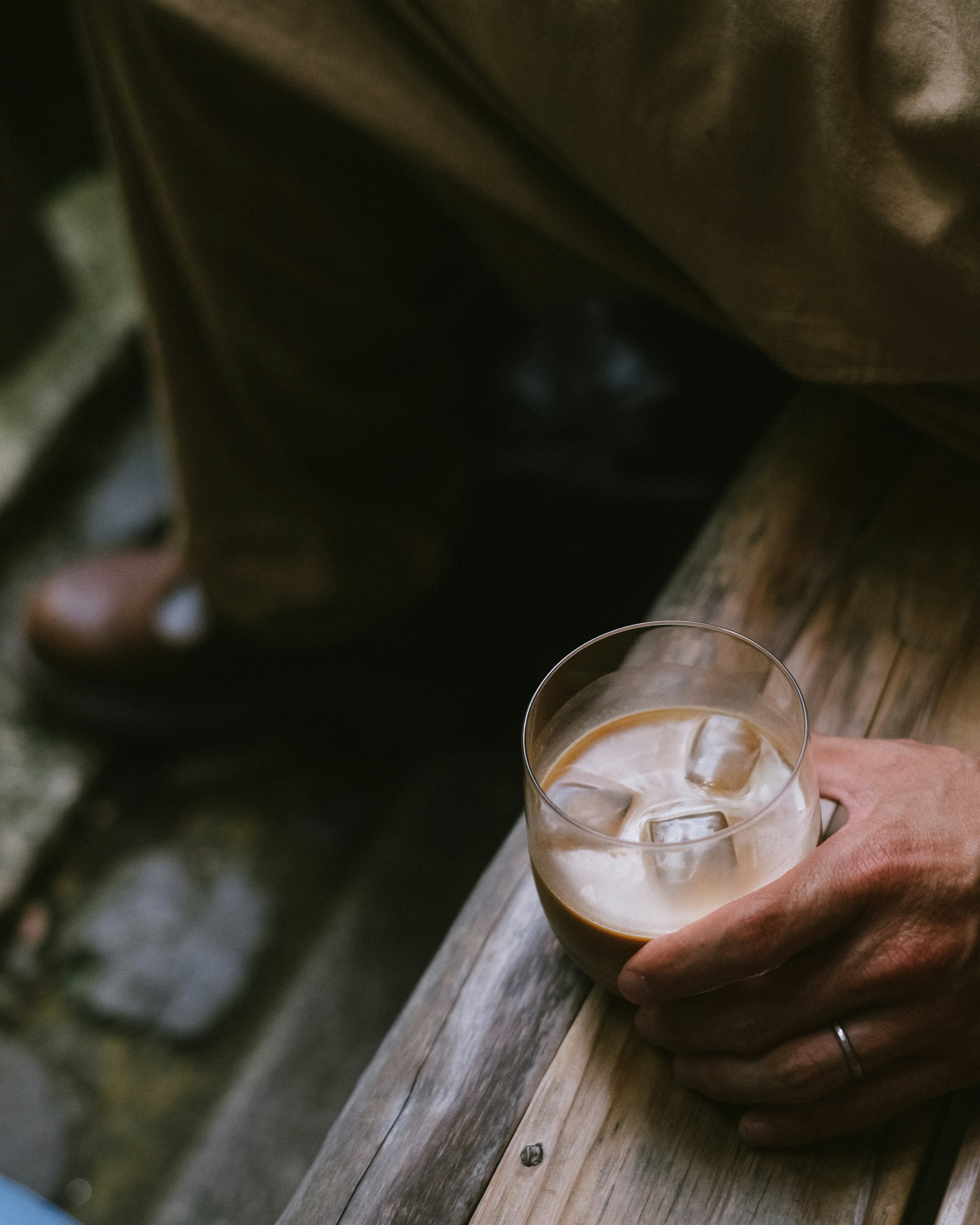 a person holding a glass of liquid on top of a wooden table