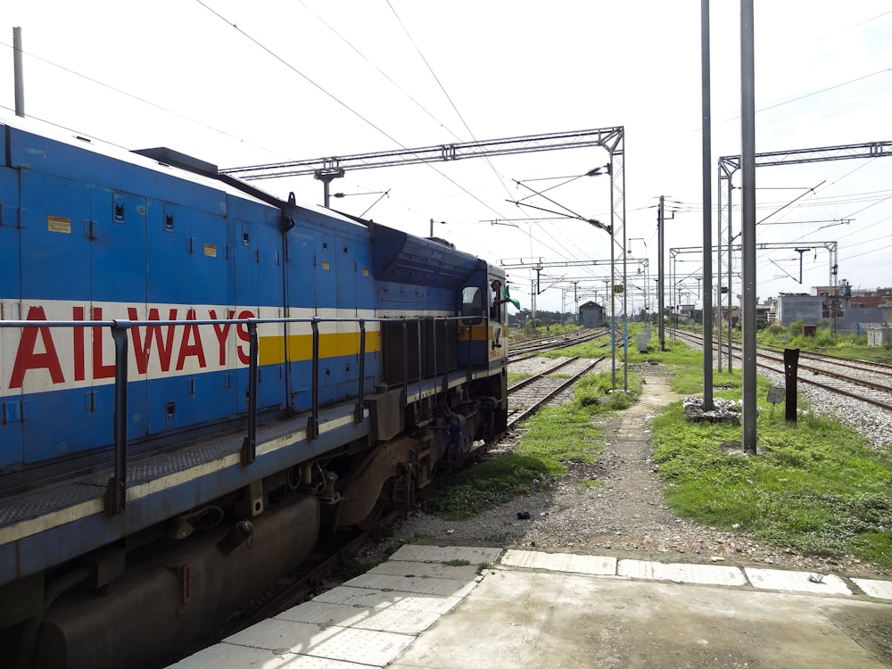 a blue train traveling down train tracks next to a lush green field