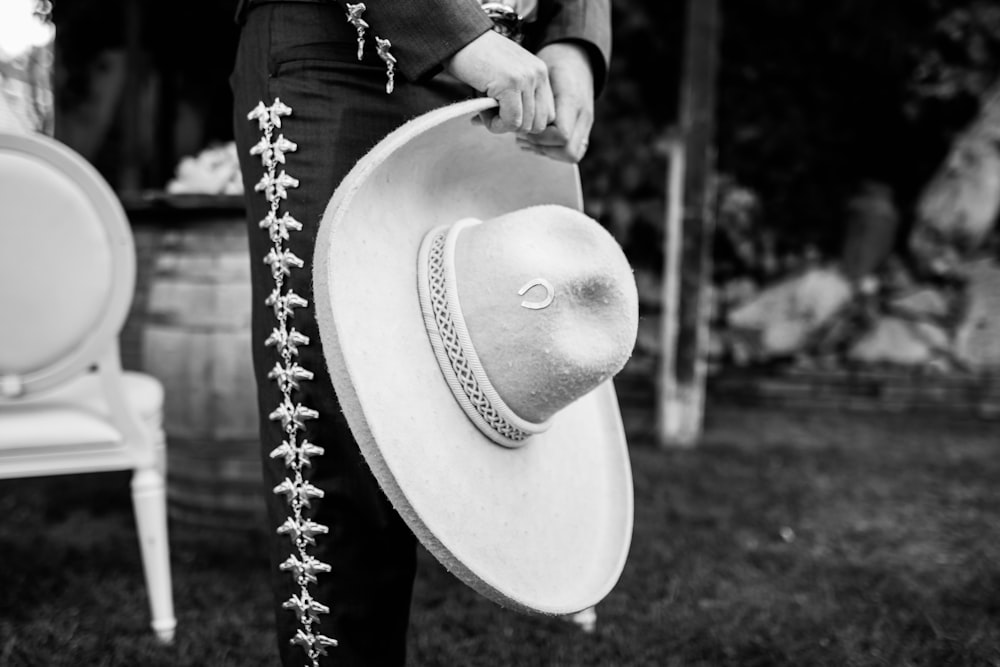 Un hombre con traje y sombrero parado junto a una silla