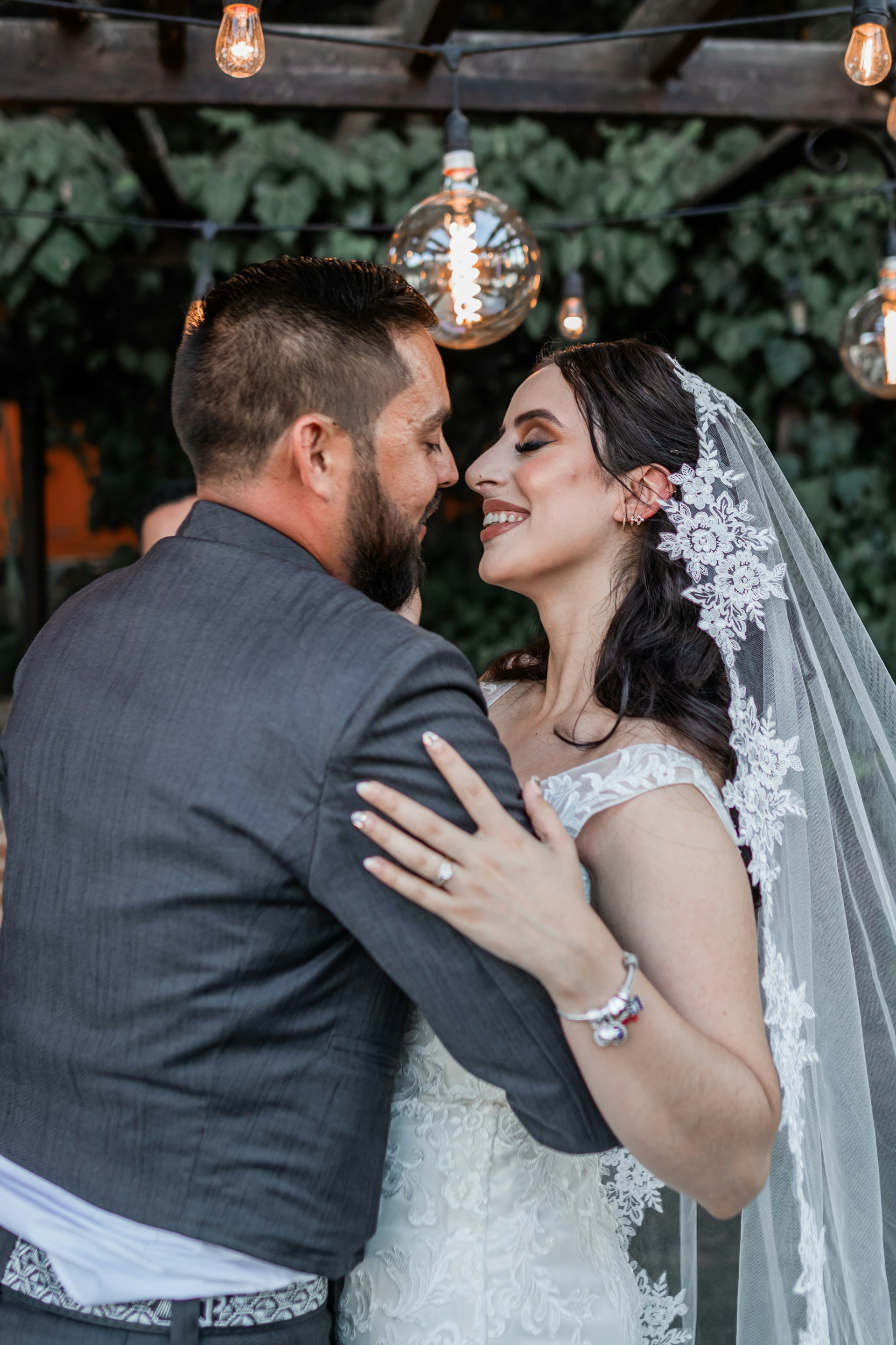 A tender moment of a bride and groom sharing laughs under twinkling fairy lights at dusk.