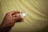 A hand is holding a SanDisk Ultra Plus 64GB memory card and its packaging against a softly blurred yellowish background. The fingers are delicately gripping the clear plastic case containing the card, which is labeled with red and white text.