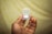A hand holding a small clear plastic case containing a memory card. The card inside is labeled with the brand name and storage capacity details. The background is blurred and features a soft yellow tone.