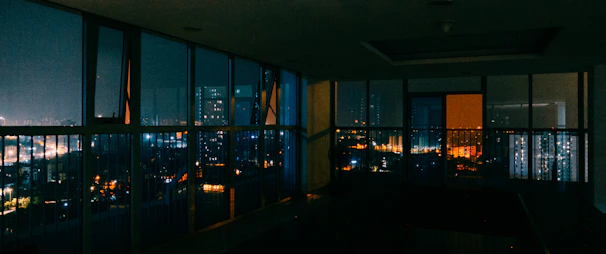 A sleek urban loft with large windows overlooking a bustling city street at dusk.