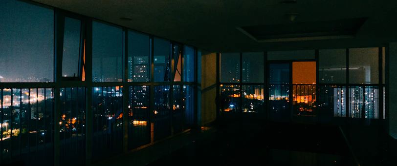 Interior of a sleek, dimly lit boardroom with platinum accents and a view of a night cityscape.