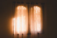 Delicate floral-patterned curtains letting warm sunlight into a quaint bedroom.