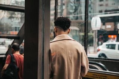 Model wearing a sophisticated beige coat with subtle gold accessories standing in natural light.