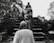 A group of individuals, some in robes, are ascending a set of stone stairs amidst ancient ruins surrounded by trees. The scene appears serene, with the forest setting and historical stones creating a sense of timelessness.