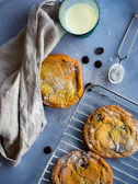 Warm chocolate chip cookies cooling on a wire rack with a glass of milk nearby.