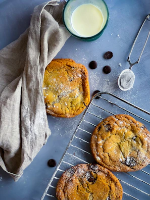 Warm chocolate chip cookies cooling on a wire rack with a glass of milk nearby.