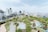 An urban park with lush green trees and pathways is surrounded by a cityscape of modern buildings and high-rises. The sky is clear, and the park features a playground area with colorful ground designs. Pedestrians and a few vehicles are visible on the adjacent streets.