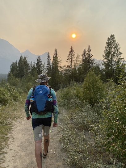 A person hiking on a forest trail carrying a backpack with camping gear under soft natural light.