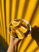 A hand holding a deep orange bowl filled with fresh fruit, highlighting the glaze texture.