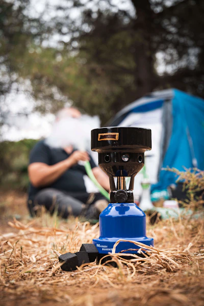 Close-up of hands setting up a durable camping stove on rocky ground beside a flowing river.