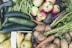An abundant assortment of fresh vegetables and fruits including cucumbers, green beans, apples, carrots, potatoes, and pears. The produce is vibrant and appears freshly harvested, with earthy tones and organic textures.