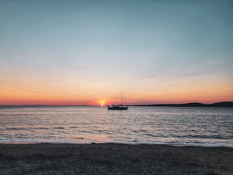 A peaceful sunset over the ocean with a yacht gently rocking in the waves.