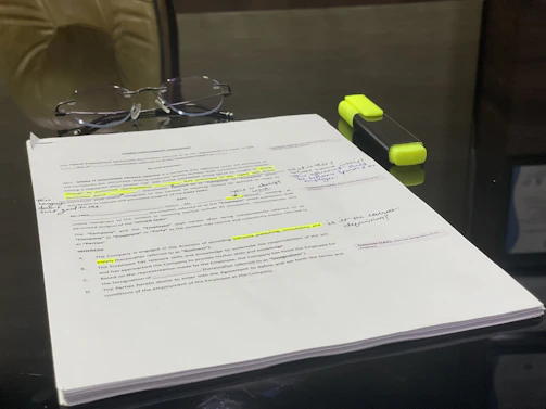 Stack of manuscripts with handwritten notes and a pair of reading glasses.