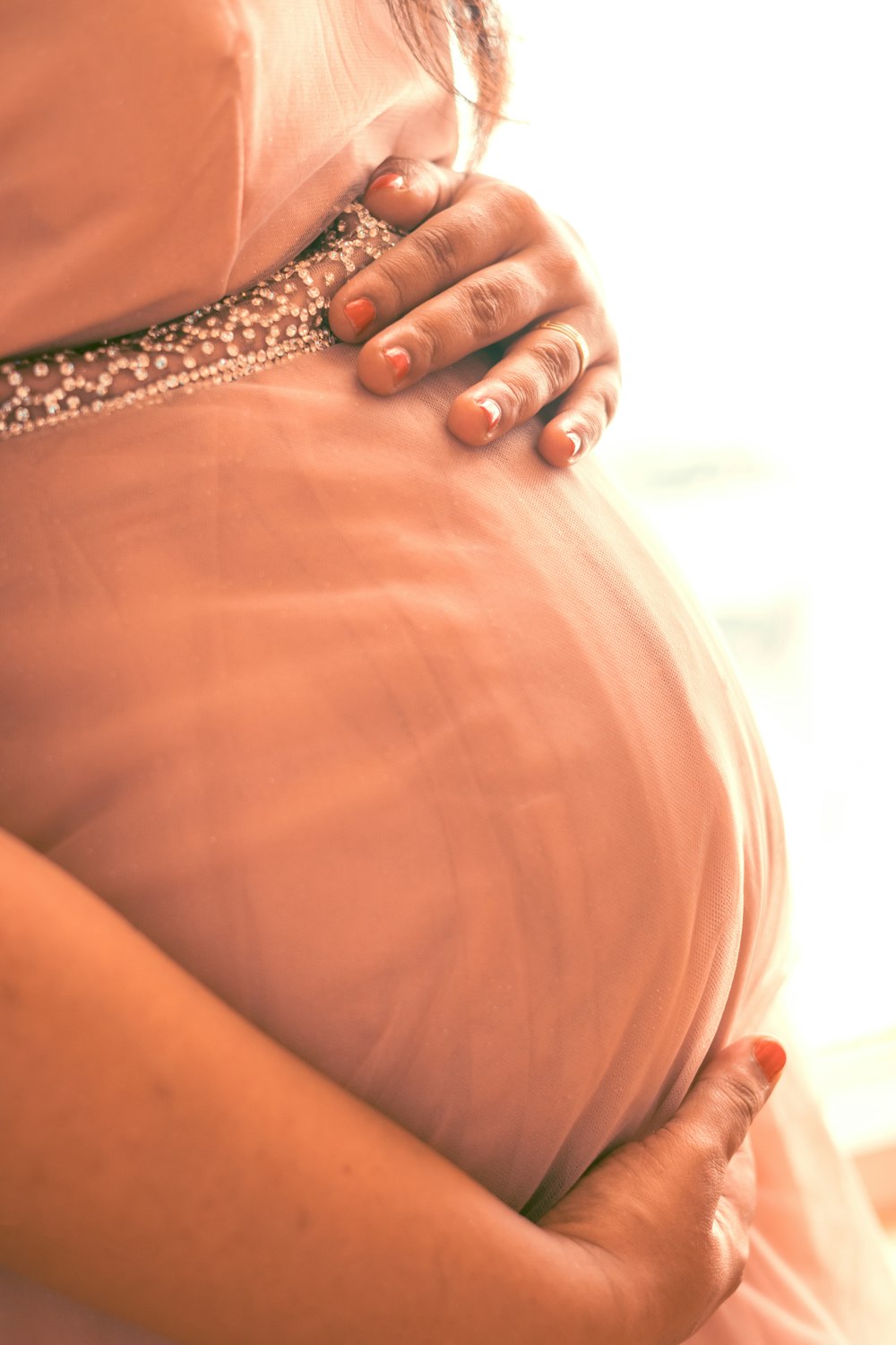 a pregnant woman in a pink dress holding her belly