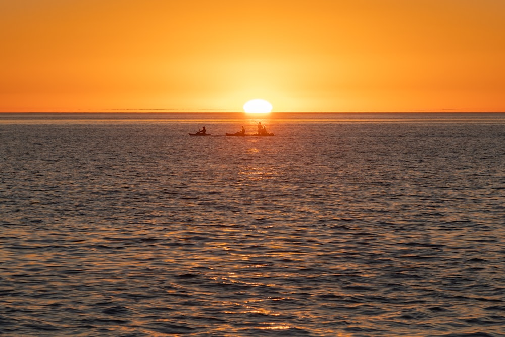 the sun is setting over the ocean with a boat in the water