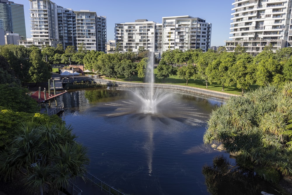 a fountain in the middle of a lake surrounded by tall buildings