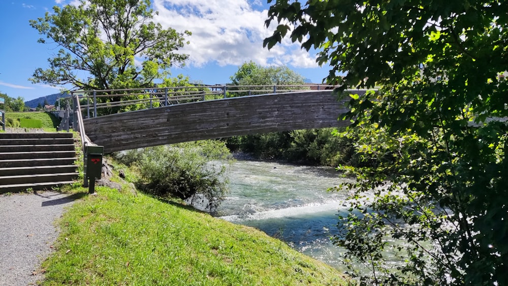 a wooden bridge over a river next to a lush green hillside