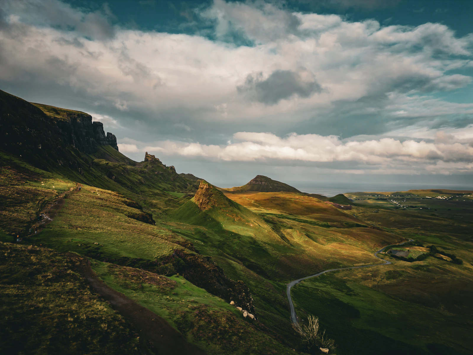 A winding single-track road cutting through the Highland mountains under a dramatic sky