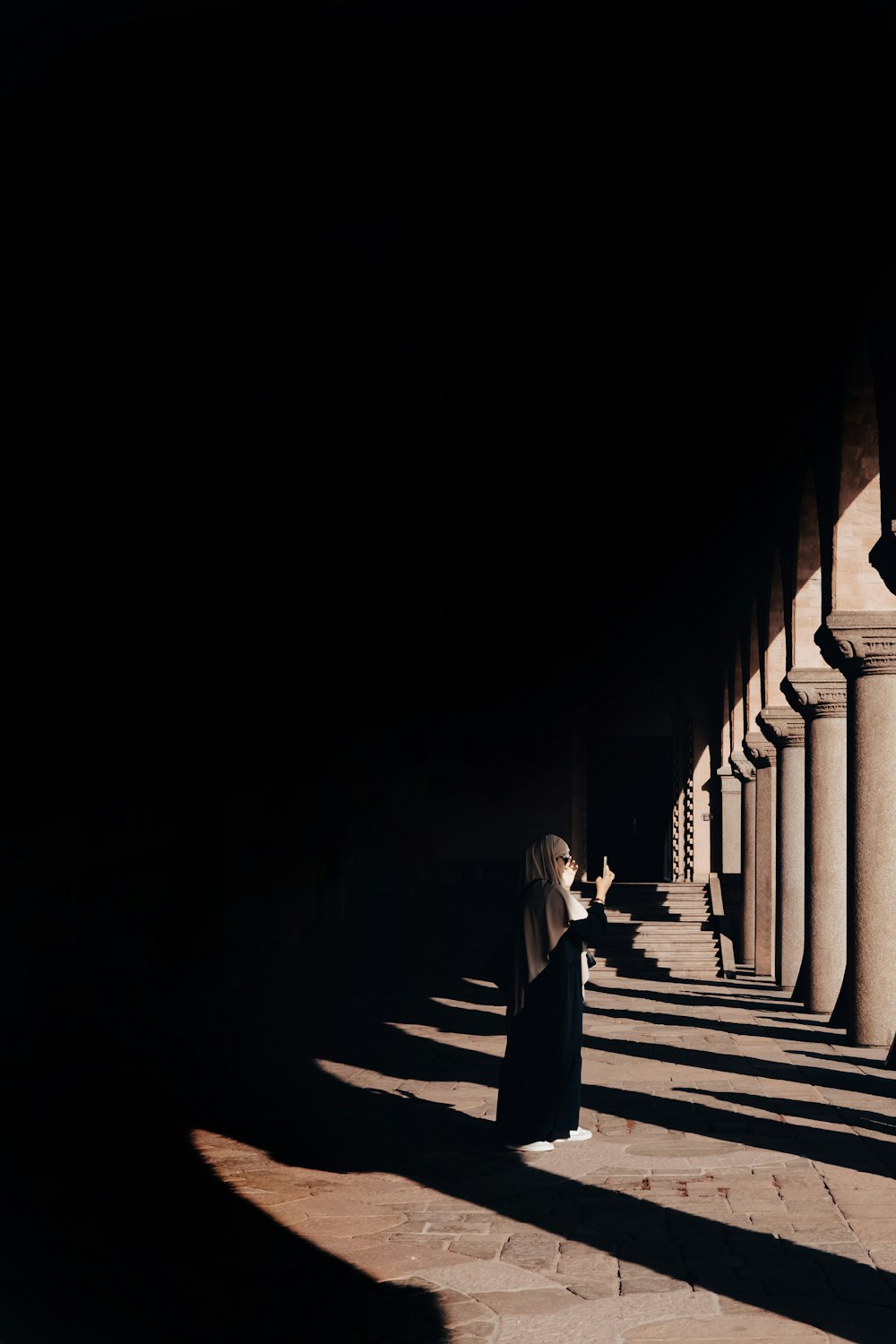 a woman in a long black dress standing in a long row of columns