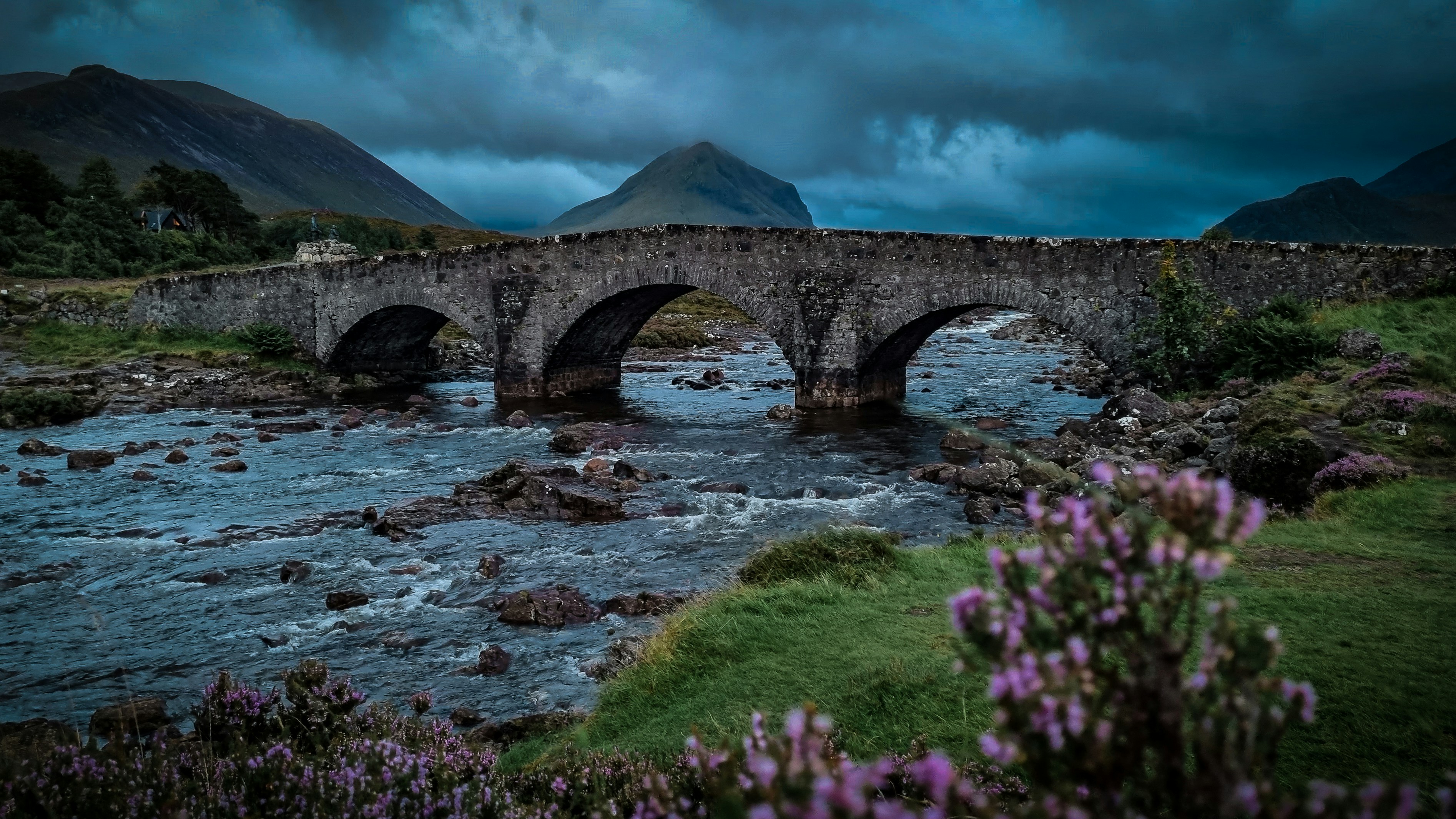 a stone bridge over a river with mountains in the background