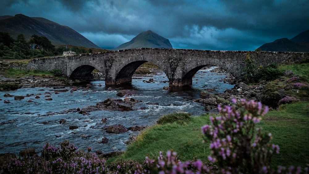 a stone bridge over a river with mountains in the background