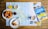On a wooden table lies a detailed map surrounded by breakfast items. Freshly baked croissants are placed on white plates, accompanied by cups of coffee and glasses of orange juice. A travel guidebook titled 'Inverness & Loch Ness' rests on the map, suggesting a planned trip to the region.