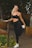 A smiling person wearing casual athletic wear holding a yoga mat outdoors.