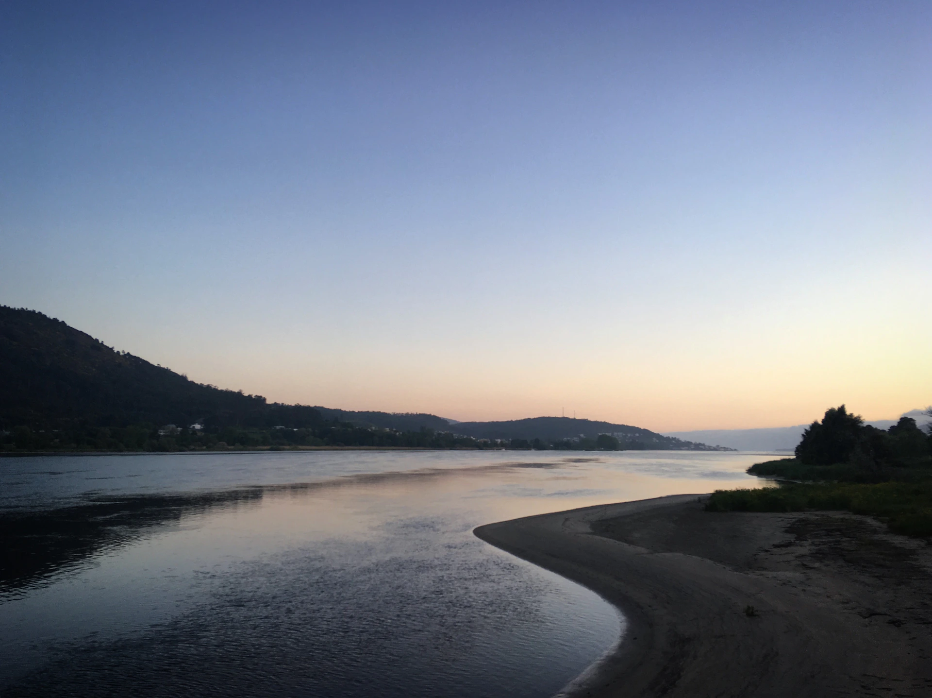 A serene view of the Ganges River flowing through Rishikesh at dawn, with soft orange and pink hues reflecting on the water.