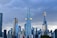 A dramatic skyline featuring several modern skyscrapers under a cloudy sky. The architecture is sleek and contemporary, with the tallest building having two prominent golden horizontal structures. The cityscape reflects a sense of urban growth and advancement.