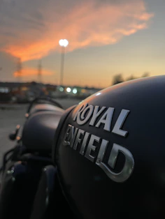 Close-up of a Royal Enfield 350 Classic Bullet parked on a rocky trail with a sunset backdrop.