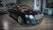 A sleek, luxurious black car with shiny chrome details is parked indoors. The vehicle features a prominent front grille and distinctive headlights. There are other cars present in the background, suggesting a showroom or garage setting. The tiled floor and wall art add to the upscale ambiance.