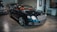 A sleek, luxurious black car with shiny chrome details is parked indoors. The vehicle features a prominent front grille and distinctive headlights. There are other cars present in the background, suggesting a showroom or garage setting. The tiled floor and wall art add to the upscale ambiance.