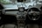The interior of a luxury car featuring a sleek dashboard with a center console screen. Prominent circular air vents and a multifunction steering wheel are visible. Through the windshield, a street view with a few pedestrians and parked cars is noticeable.
