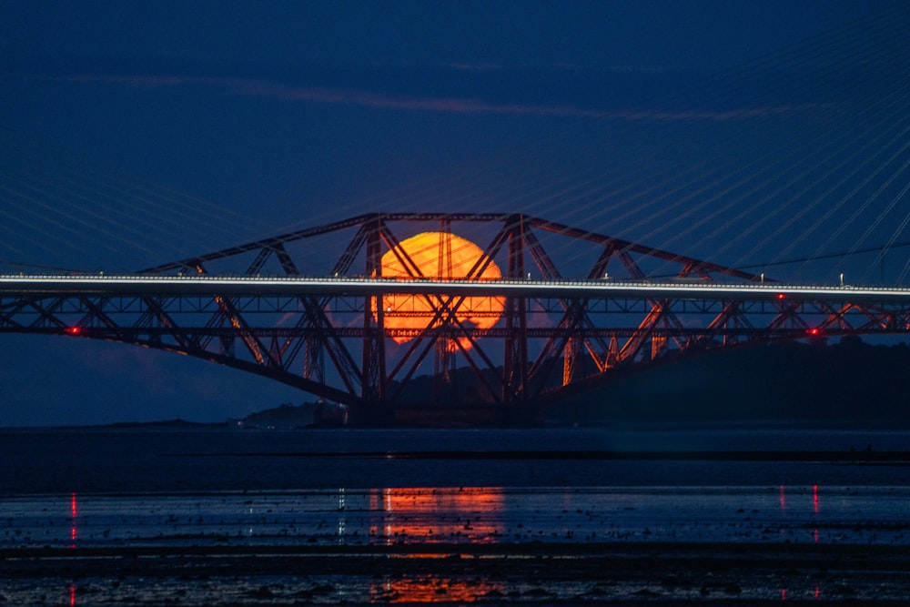 a full moon is seen behind a bridge