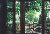 A quiet street café scene with soft white chairs and a gentle breeze moving sheer curtains.
