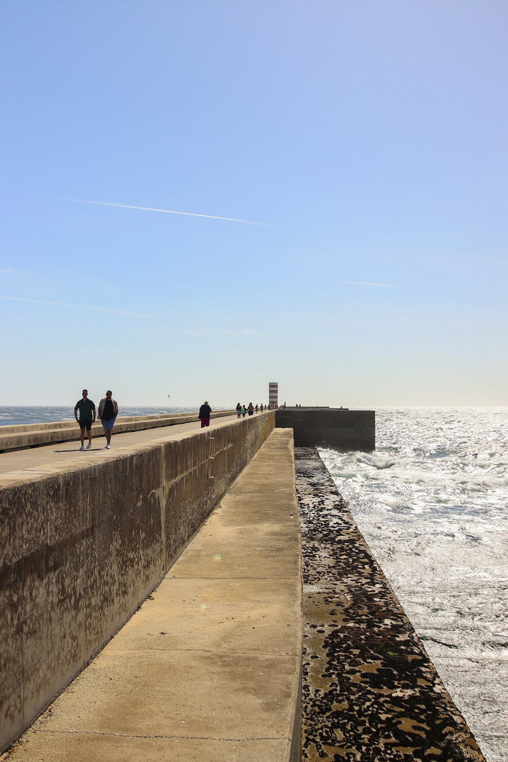 a group of people walking along a pier next to the ocean