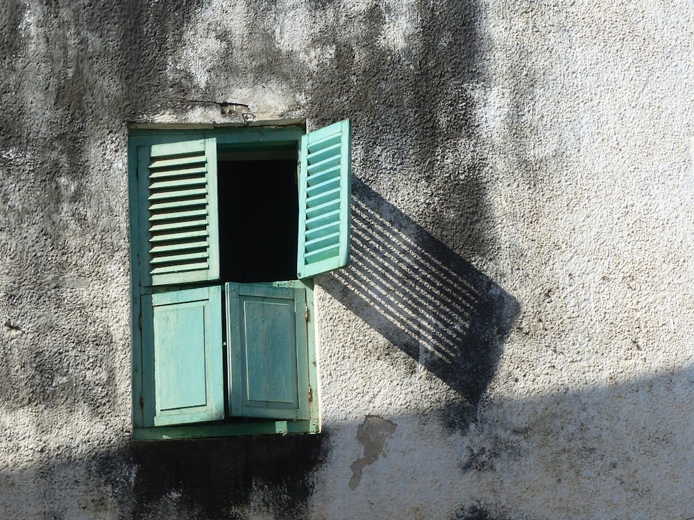 a green shuttered window with a shadow cast on the wall