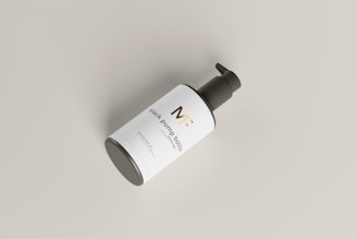 A black pump bottle is placed at an angle against a light gray background. The bottle has a sleek design with a white label featuring gold and black text. The pump top is black and contrasts with the clean and minimalist look of the label and bottle.