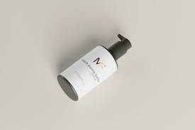 A black pump bottle is placed at an angle against a light gray background. The bottle has a sleek design with a white label featuring gold and black text. The pump top is black and contrasts with the clean and minimalist look of the label and bottle.