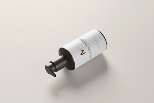 A sleek black pump bottle with a white label lies on a light-colored surface. The label features minimalist text and design elements, giving a modern and clean aesthetic.