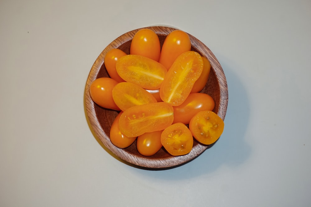 a wooden bowl filled with lots of orange tomatoes