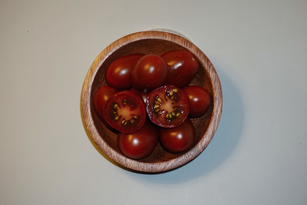 a wooden bowl filled with tomatoes on top of a table
