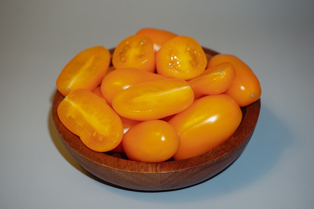 a wooden bowl filled with orange tomatoes on top of a table